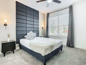 A modern bedroom with a large bed, a dark headboard, bedside lamps, a nightstand, and a window with curtains. - Theme Park Villa: Pool, Game Room, Family Getaway! (Davenport)