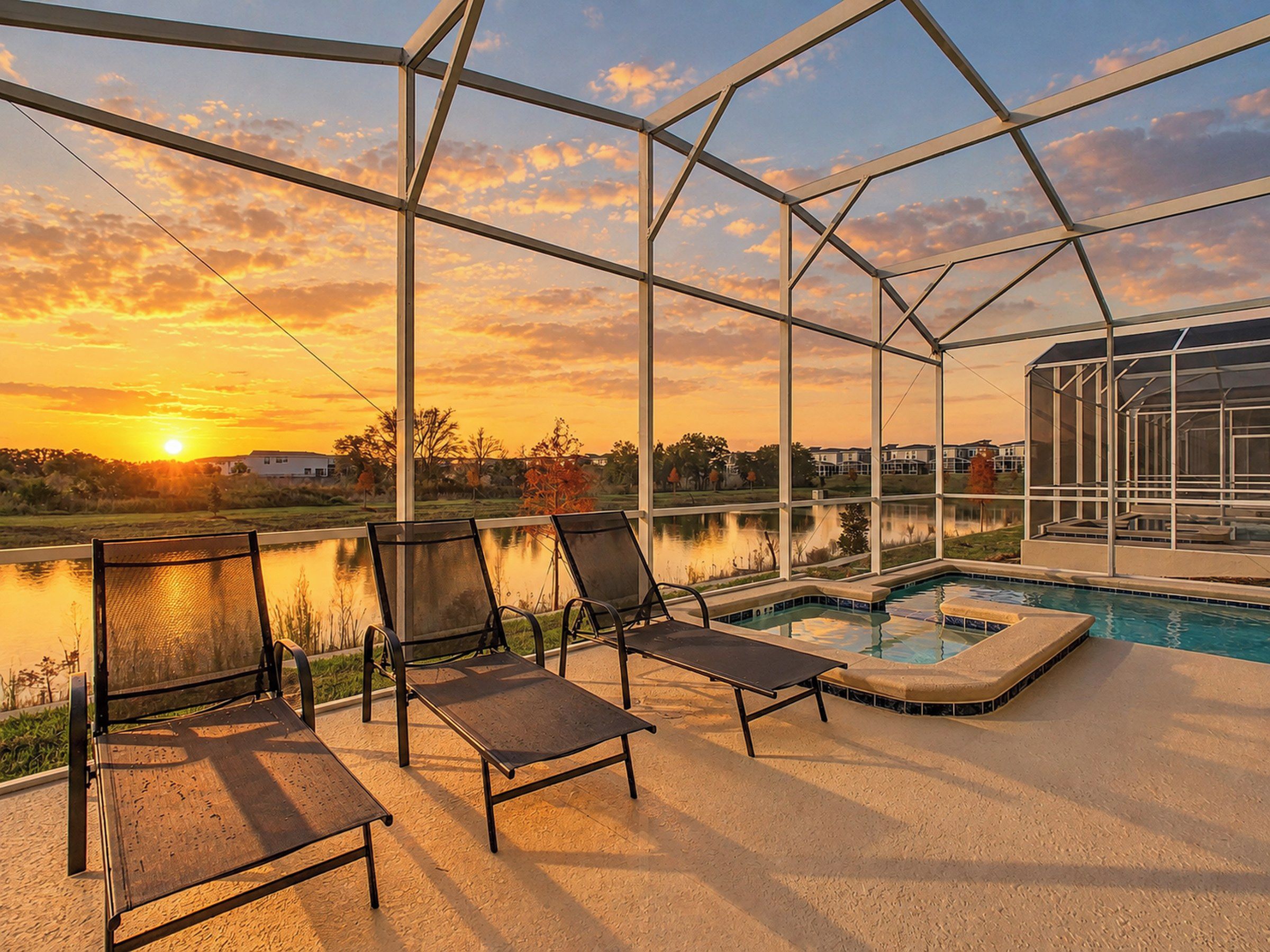 Un espacio exterior techado con piscina, sillas de descanso y vistas al atardecer sobre el agua.