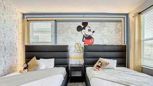 A hotel room with two beds, a Mickey Mouse mural on the wall, and a window with blinds.