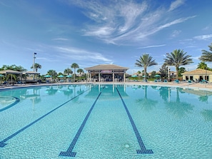 Piscina com várias pistas, cercada por espreguiçadeiras e guarda-sóis, com um bar ao fundo.