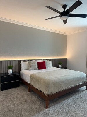 A bedroom with a bed, a nightstand, a ceiling fan, and a wall-mounted light.