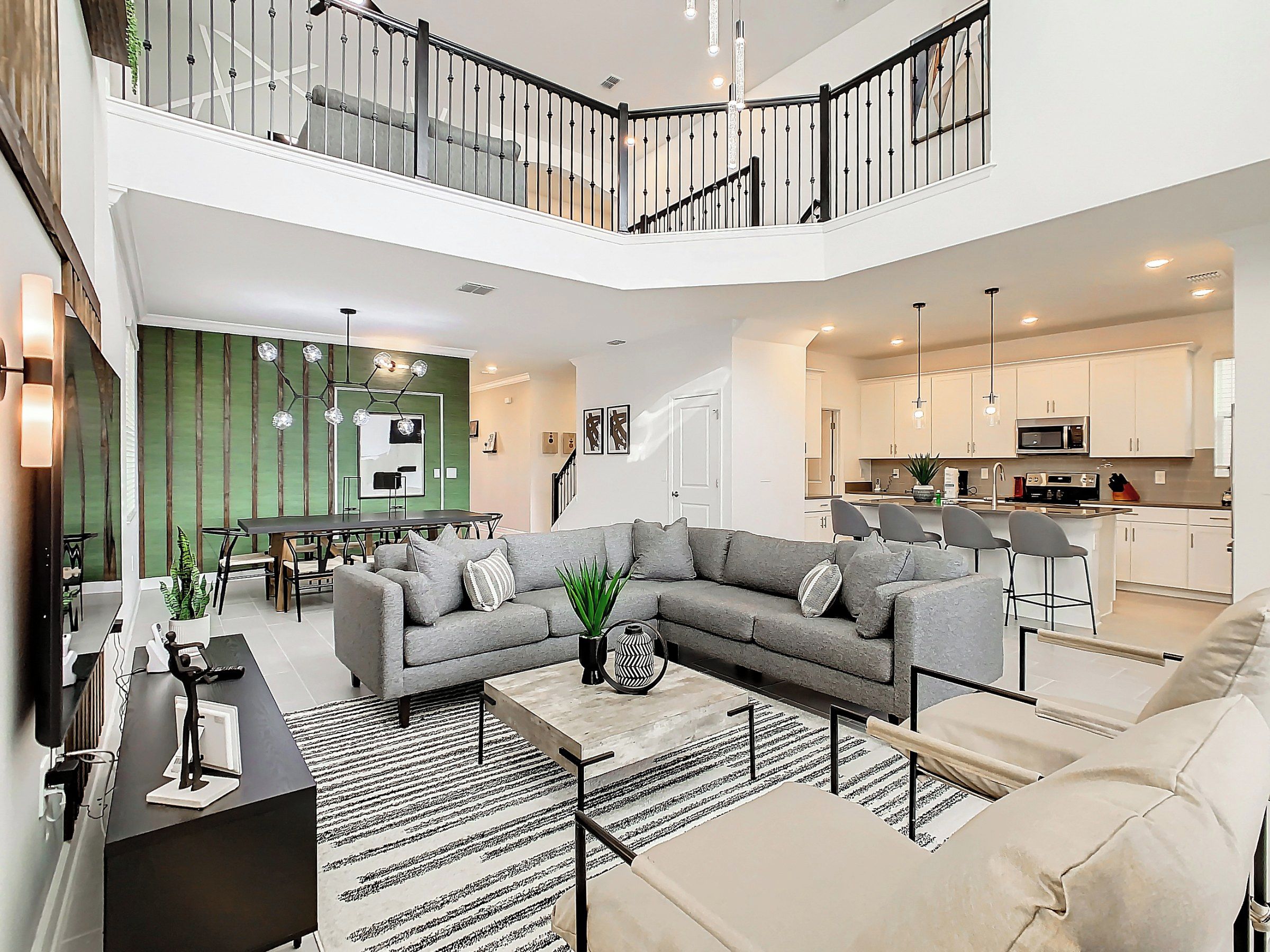 A spacious living area with a grey sectional sofa, a coffee table, and a dining area with a green accent wall.