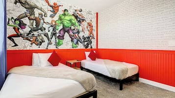 Une chambre d’hôtel avec deux lits, un mur d’accent rouge et une grande fresque murale sur le thème des super-héros.