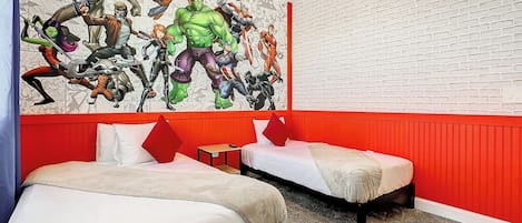 A hotel room with two beds, a red accent wall, and a large superhero-themed mural.