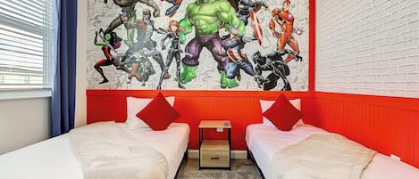 Habitación de hotel con dos camas, una pared de acento roja y un mural grande con temática de superhéroes.
