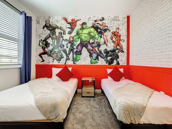 A hotel room with two beds, a red accent wall, and a large superhero-themed mural.