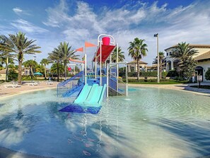 A water park with a water slide, palm trees, and a pool.