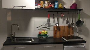 Cozinha compacta com pia, pequena geladeira e bancada com diversos utensílios de cozinha.