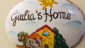 Um azulejo de cerâmica com o texto 'Giulia's Home' e um desenho de uma casa com um sol acima.