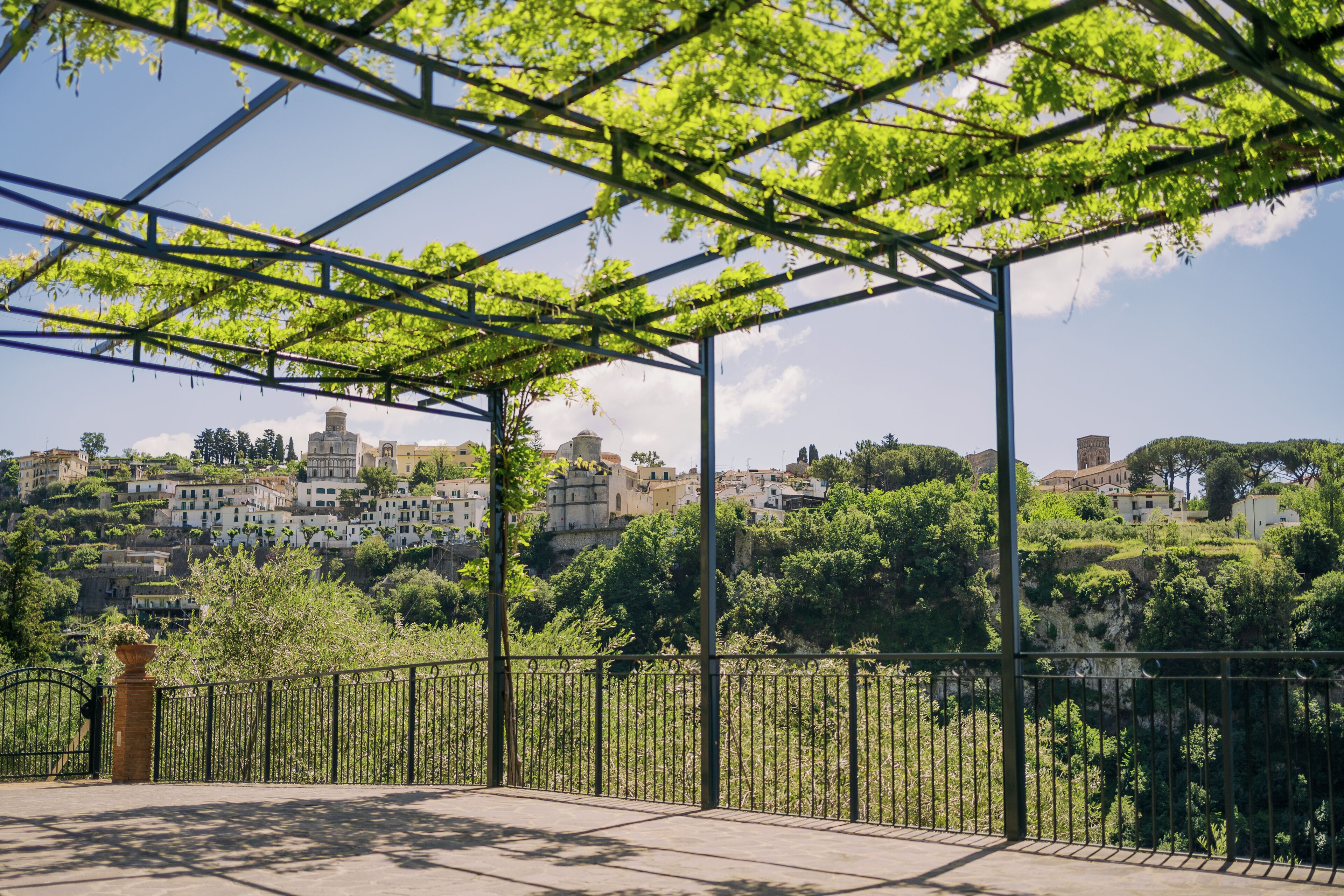 Un espace extérieur abrité, doté d’une rambarde en métal, de verdure et offrant une vue sur une ville située sur une colline.