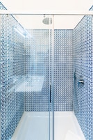 Un baño moderno con un patrón geométrico de azulejos, cabina de ducha de vidrio y bañera blanca.