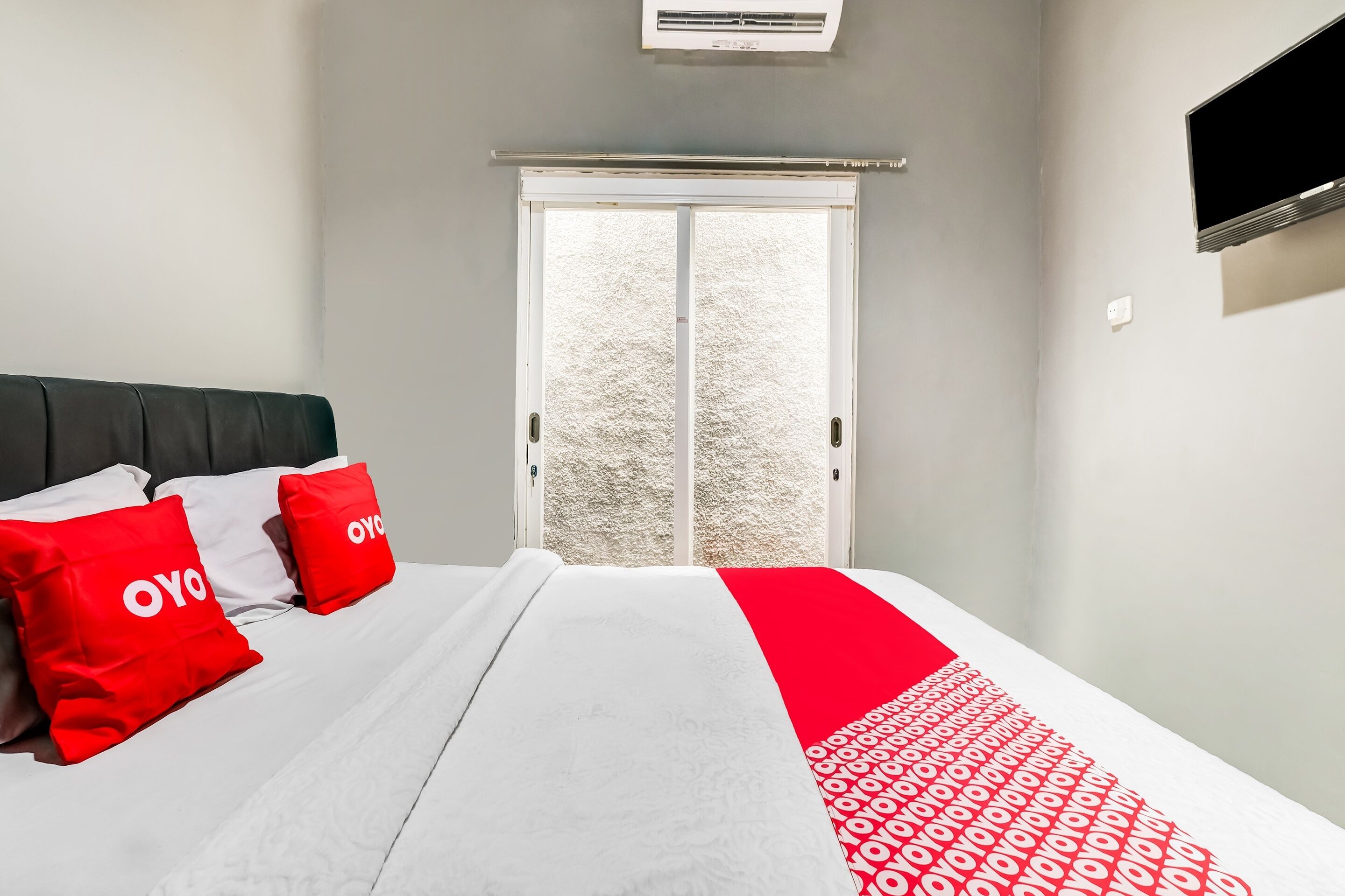 A hotel room with a bed, a TV mounted on the wall, and a sliding glass door leading to a balcony.