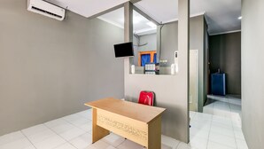 A room with a wooden desk, a red chair, a flat-screen TV mounted on the wall, and a mirror above the desk. - OYO Life 91239 Kost Rosandy House Yogyakarta (Ngaglik)