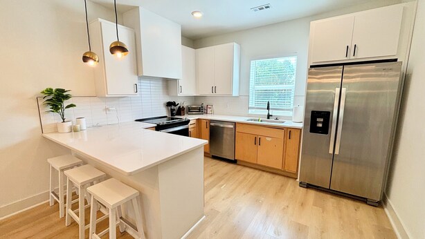 A modern kitchen with white cabinetry, a stainless steel refrigerator, a central island with bar stools, and pendant lighting. - Air-hockey garage game room, 3 queen bedrooms, sleeps 10 — 5 min to BNA, near Opry Mills (Nashvillle)