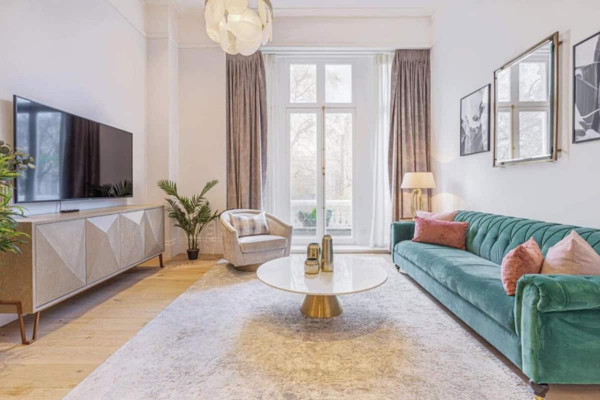 Een moderne woonkamer met een groene bank, een witte fauteuil, een ronde salontafel en een tv op een kast.