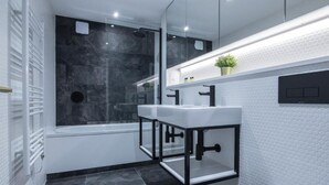 Une salle de bain moderne avec une douche à parois de verre, des murs recouverts de carreaux blancs et un lavabo encadré de noir.