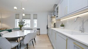 Une cuisine moderne avec des armoires blanches, un comptoir en marbre et un robinet en acier inoxydable. On y trouve également un coin repas avec une table ronde et des chaises.