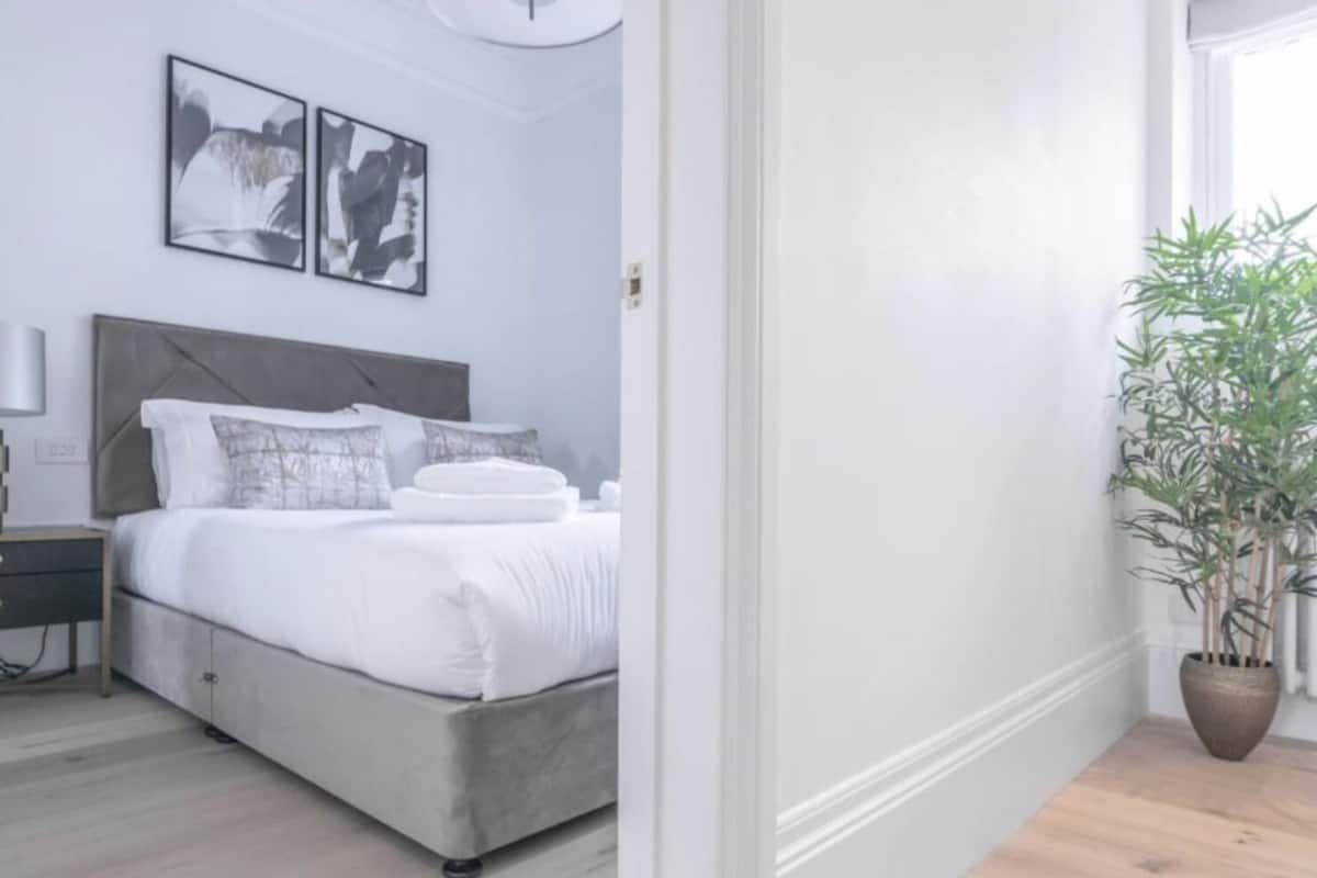 Een slaapkamer met een bed, nachtkastje, lamp en een potplant.