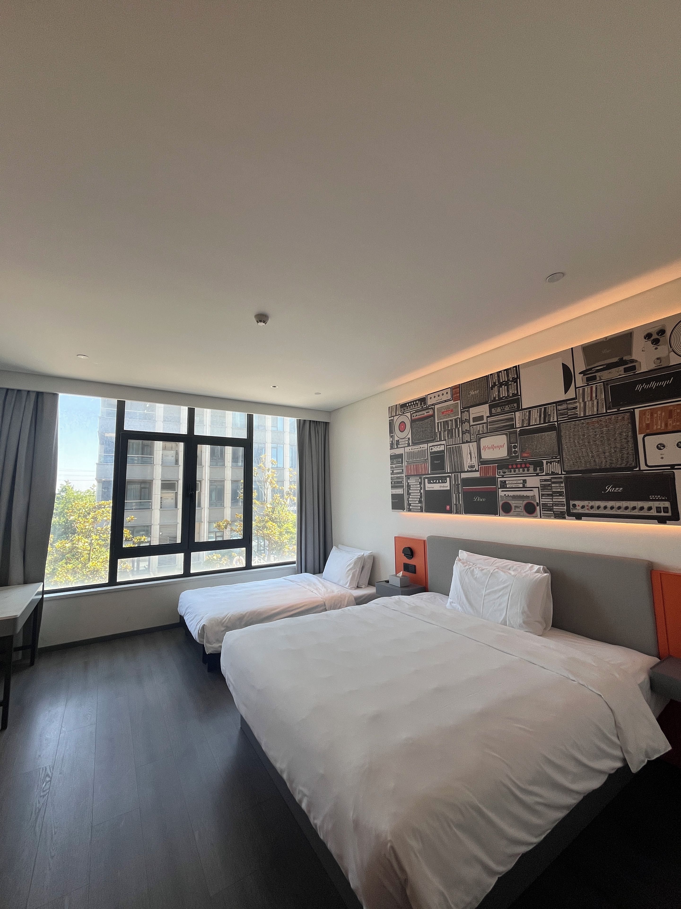 A hotel room with two beds, a desk, and a large window.