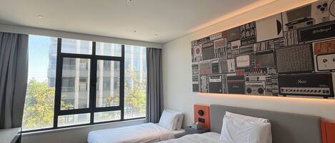 A hotel room with two beds, a desk, and a large window.