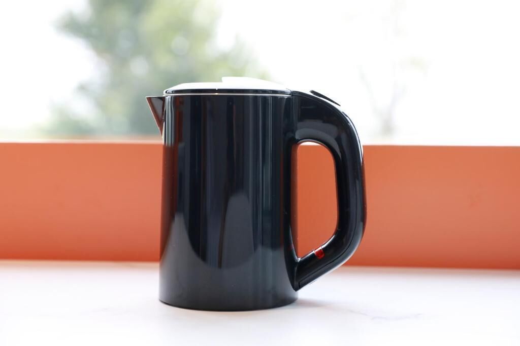 Uma chaleira preta sobre uma superfície branca com um fundo laranja.