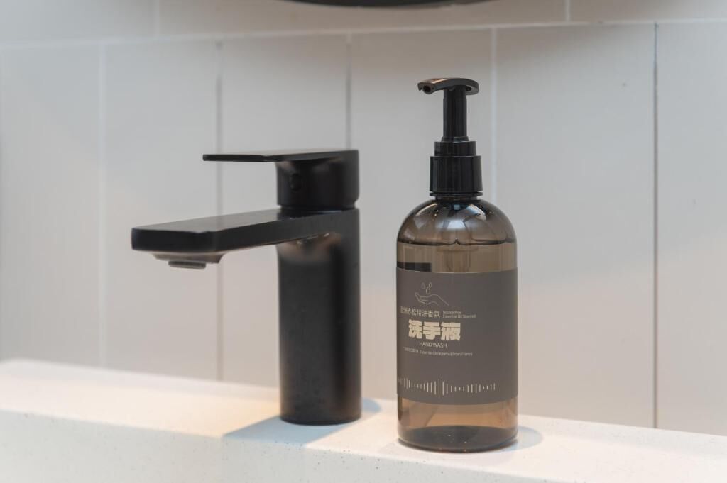 A bathroom with a black faucet and a clear bottle of hand wash soap.
