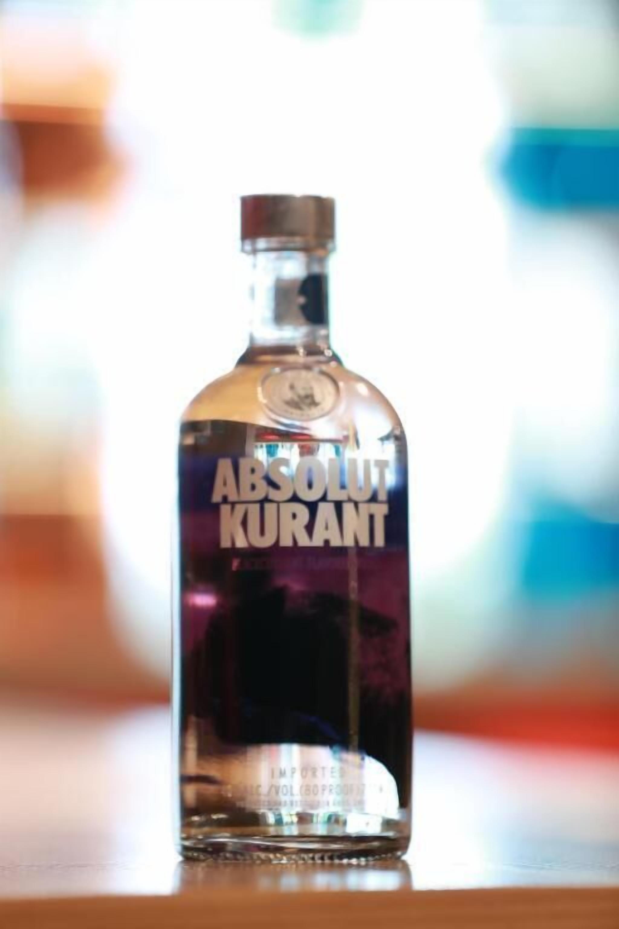Una botella de Absolut Kurant sobre una superficie reflectante.