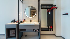 Une salle de bain moderne avec un lavabo blanc, un miroir rond et un espace douche doté d’un porte-serviettes.