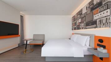 A modern hotel room with a large bed, a small table, a TV, and a wall decorated with vintage audio equipment.