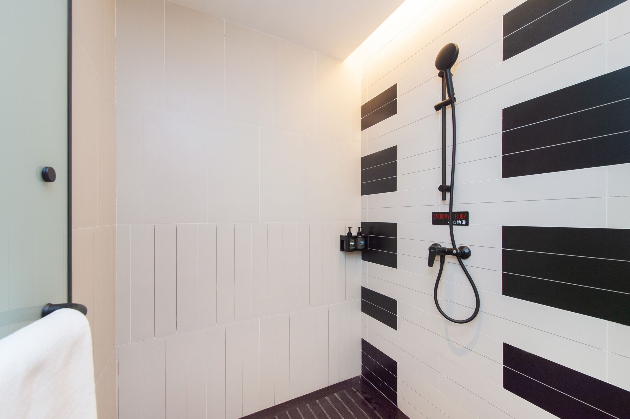 A bathroom with white and black tiles, a shower with a handheld showerhead, and a towel rack.