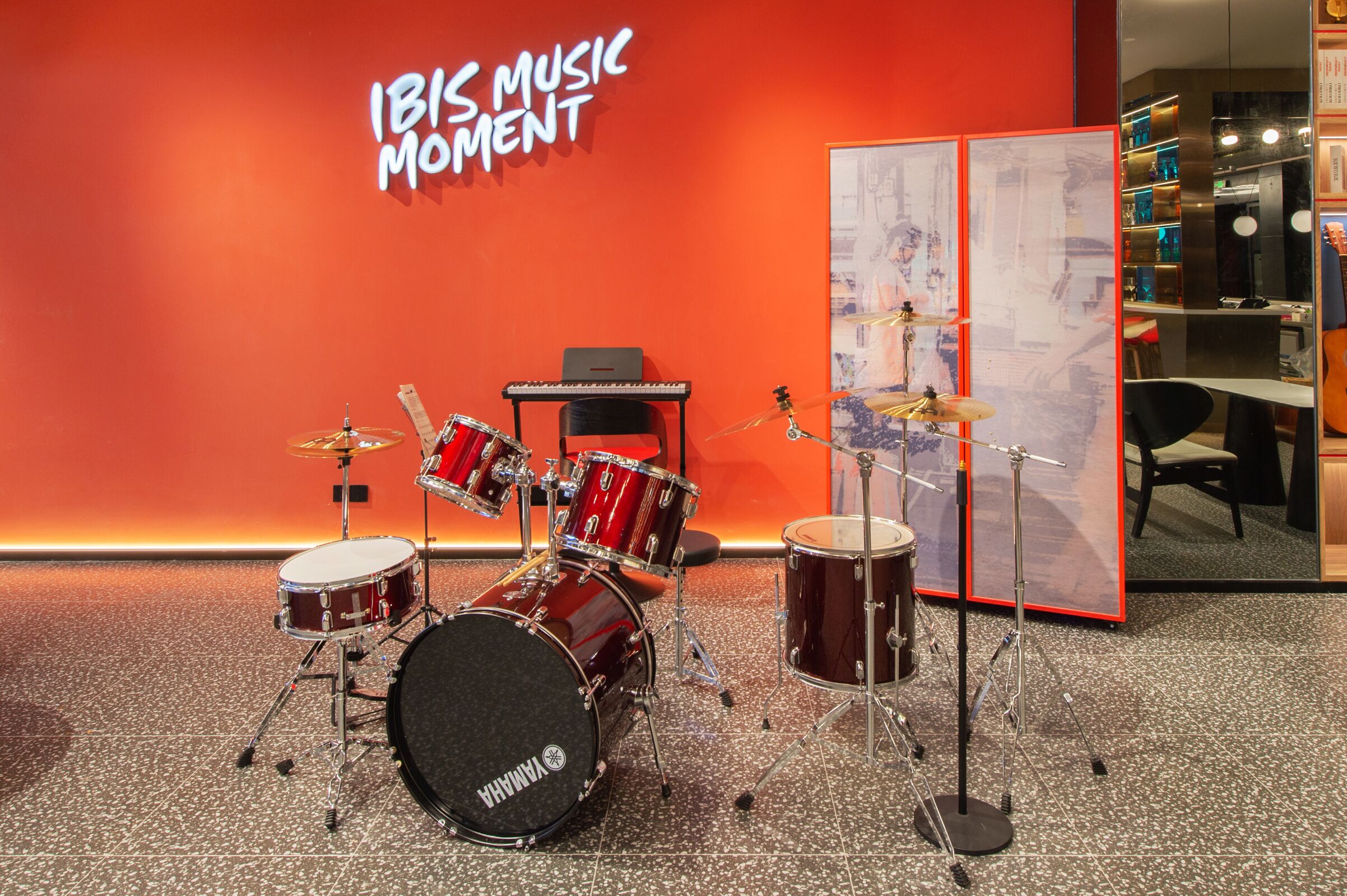 A drum set in a room with a red wall and a sign that reads "IBIS MUSIC MOMENT".