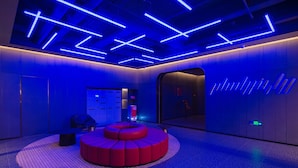 Un hall d’entrée moderne avec un espace de détente circulaire aux sièges rouges, un comptoir d’accueil et un kiosque d’information numérique.