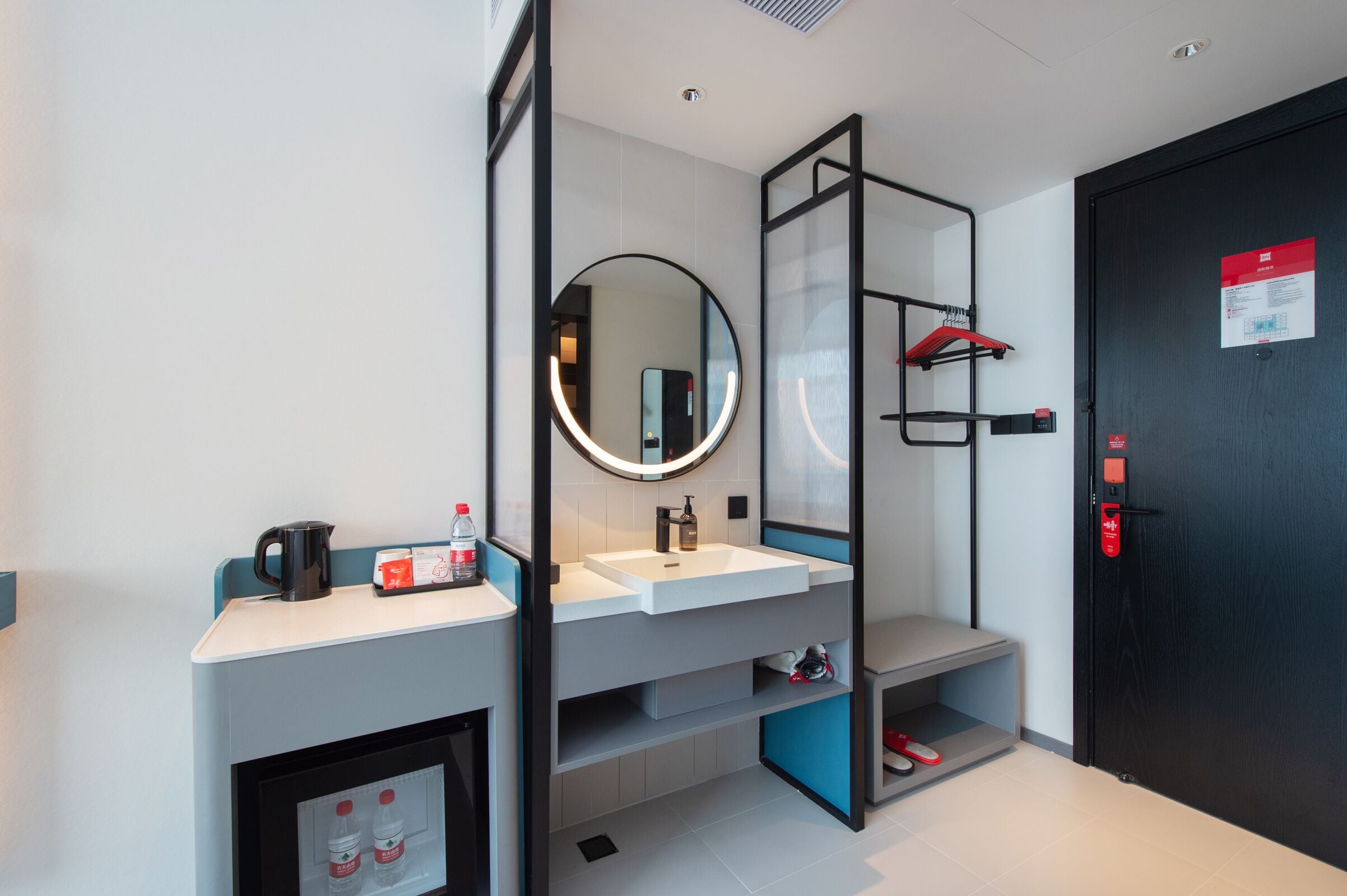 A modern bathroom with a white sink, a mirror, a shower area, and a door with a red emergency button.