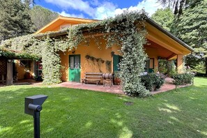 A rustic building with a green door, a bench, and a barrel in the front yard.