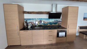 Cocina moderna con armarios de madera, encimera negra, extractor de acero inoxidable y un mural con vistas panorámicas.