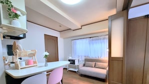 Un espace de vie compact comprenant un coin cuisine, un coin repas avec des chaises, un canapé et une fenêtre avec des rideaux.