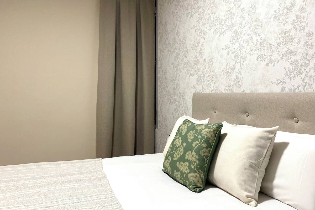 Ein Hotelzimmer mit einem Bett, beigen Vorhängen und blumigem Wandpapier.