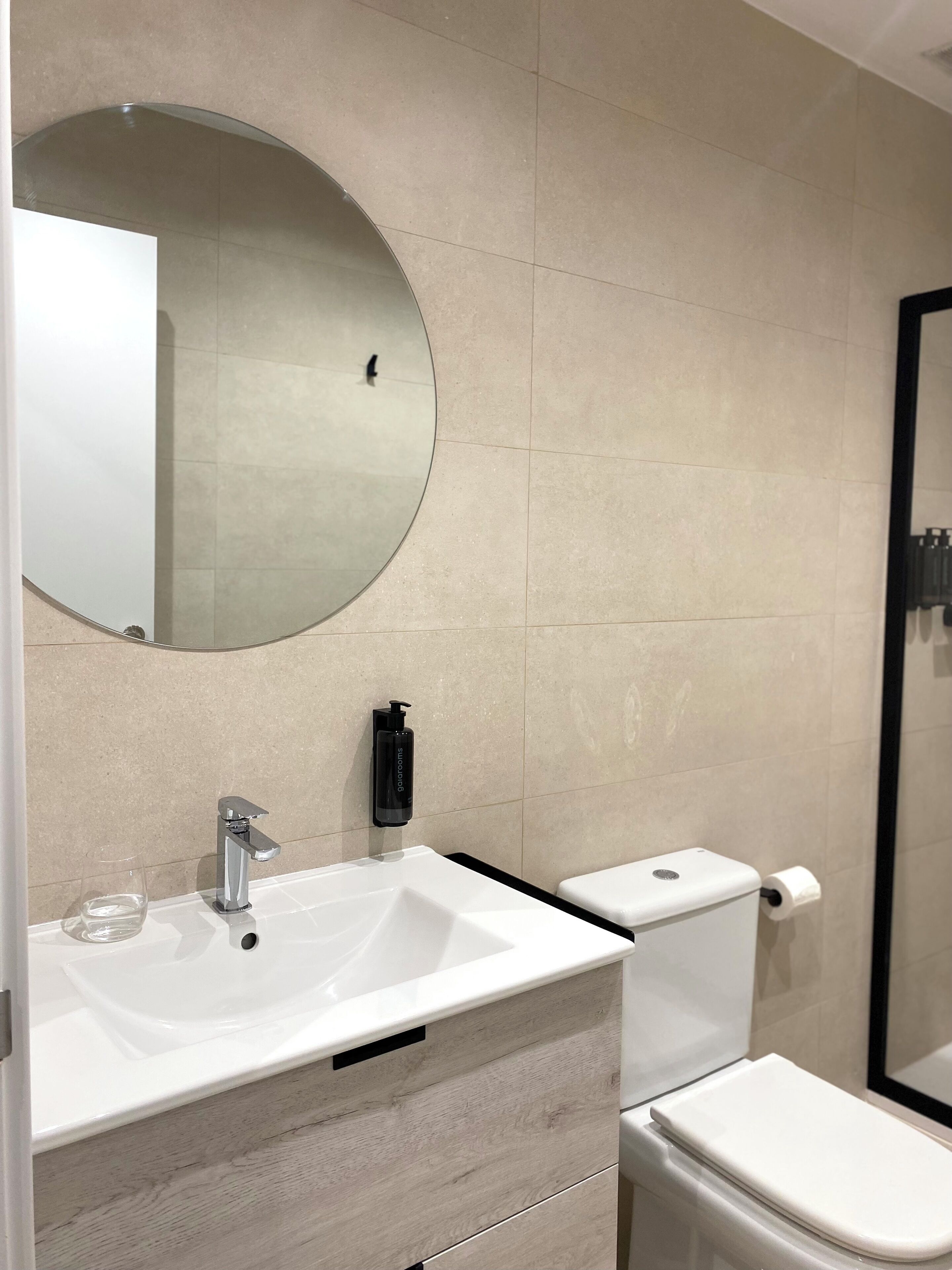 Un bagno moderno con lavandino bianco, specchio, servizi igienici e dispenser per sapone.