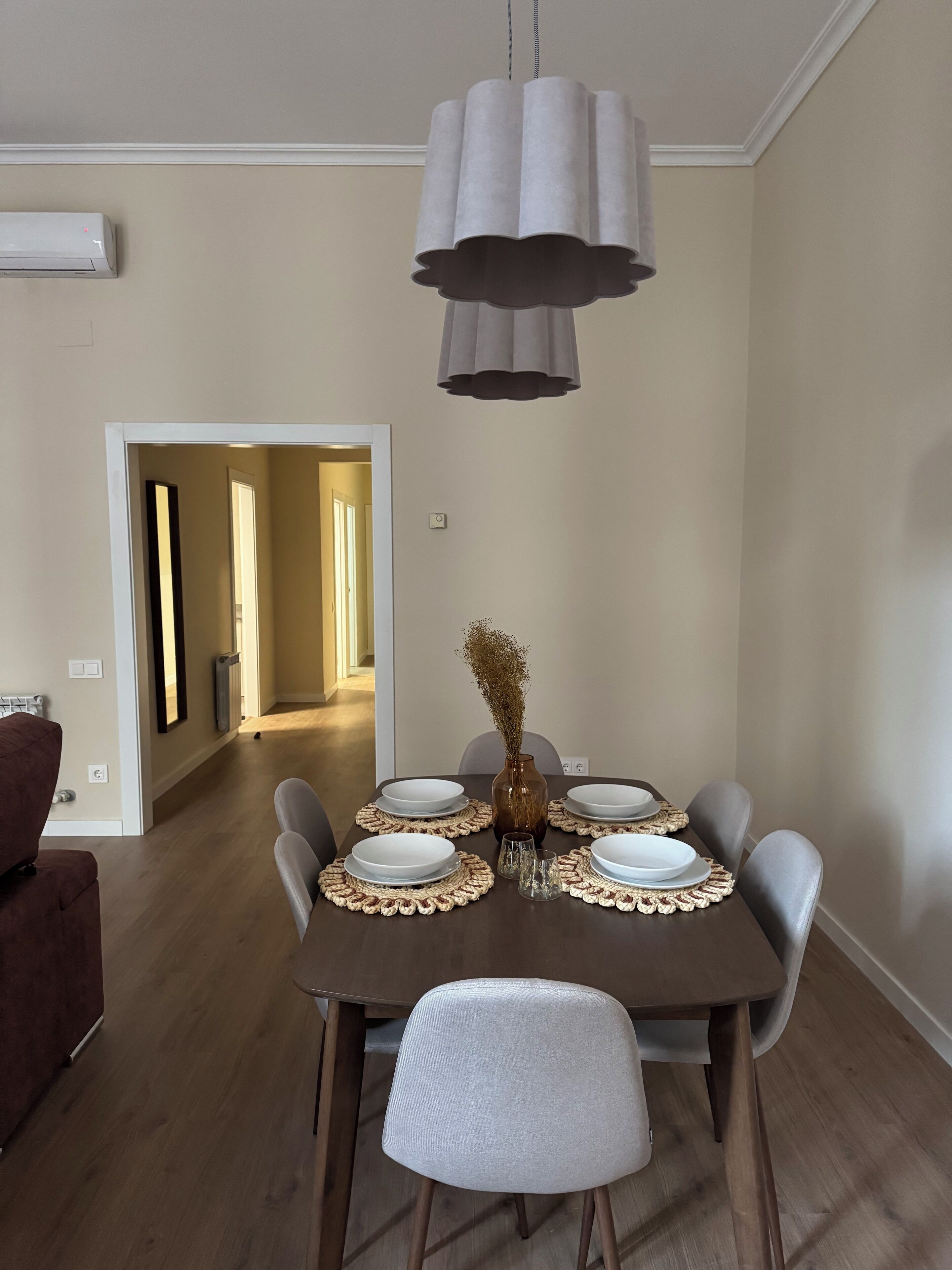 A dining area with a table set for four, a vase with dried flowers, and a pendant light.