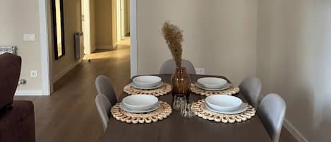 A dining area with a table set for four, a vase with dried flowers, and a pendant light.