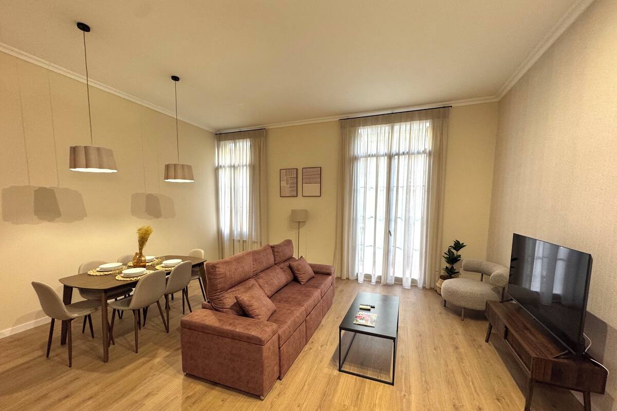 Ein modernes Wohnzimmer mit braunem Sofa, Esstisch und Stühlen. Es gibt einen Flachbildfernseher und einen Couchtisch.
