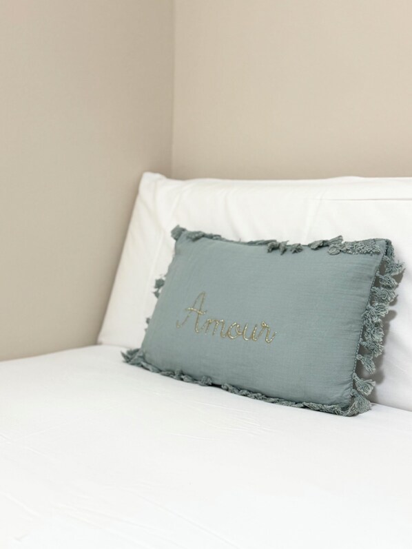 A pillow with the word "Amour" embroidered on it, placed on a white sofa.
