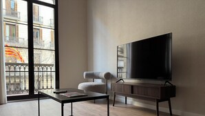 A modern living room with a large flat-screen TV, a minimalist coffee table, and a comfortable armchair. - Anais Apartments by gaiarooms  (Barcelona)