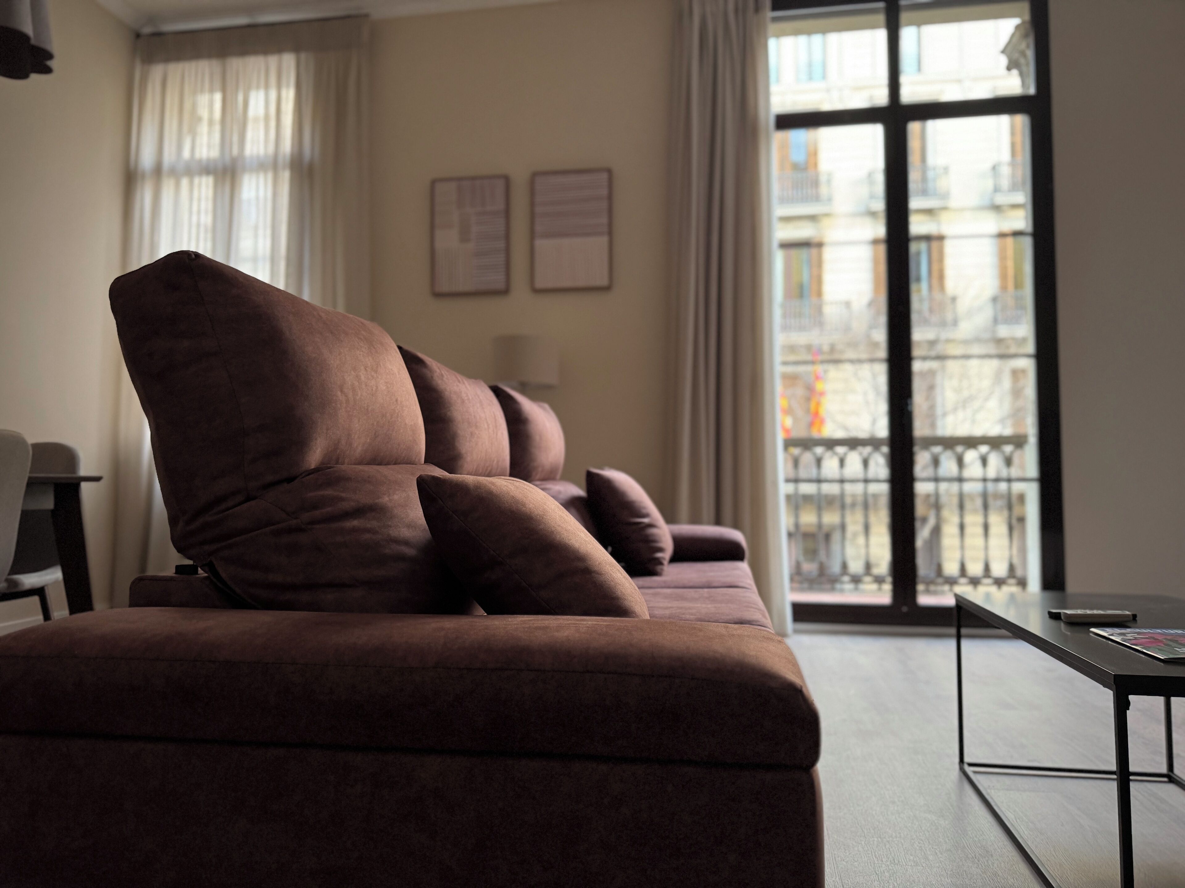 A modern living room with a brown sofa, a small table, and a view of buildings through a window.