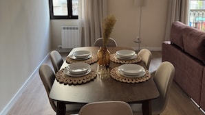 A dining area with a table set for four, a vase with dried flowers, and a sofa in the background. - Anais Apartments by gaiarooms  (Barcelona)