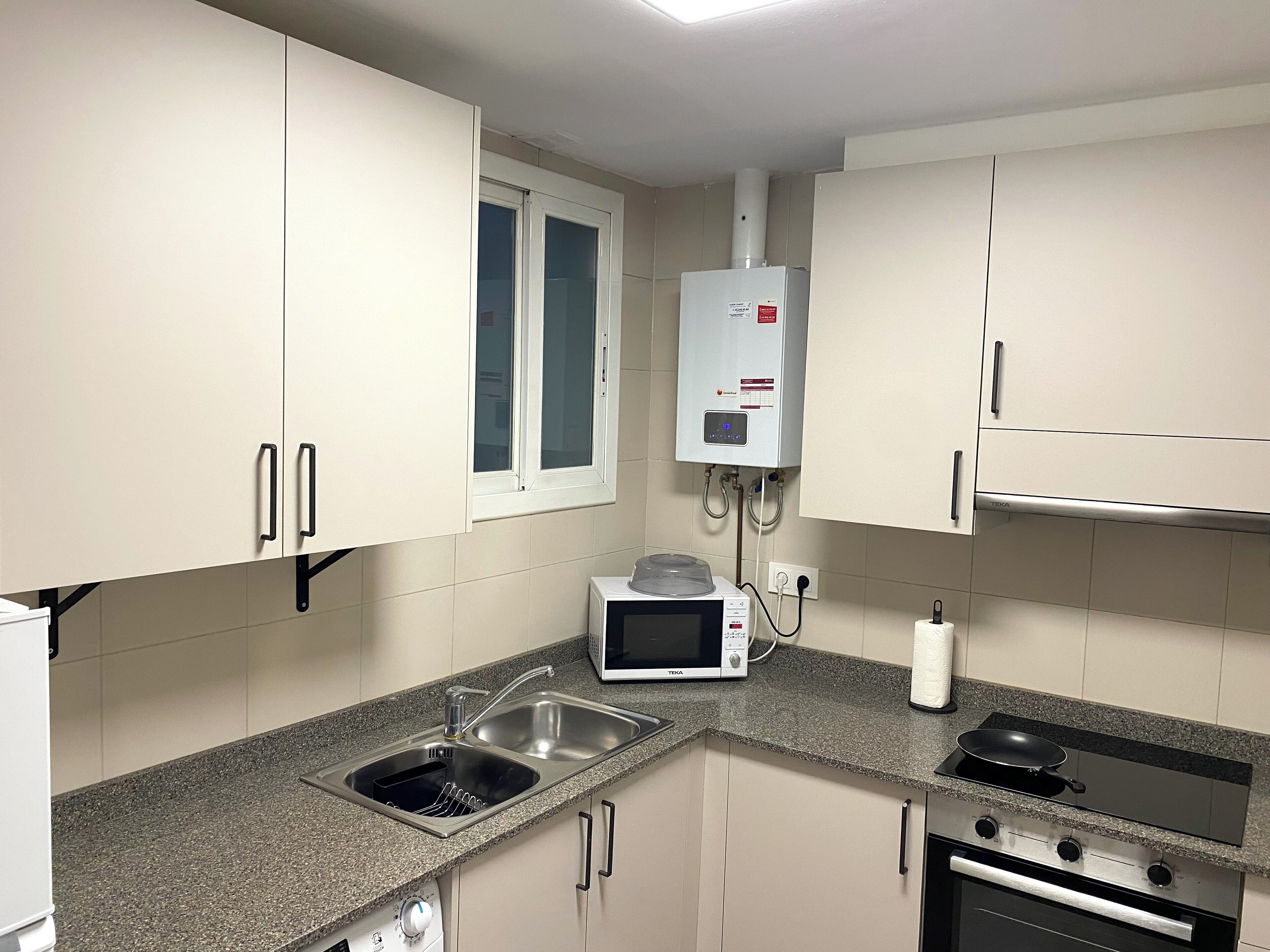 Una cucina moderna con mobili bianchi, forno a microonde integrato, piano cottura e lavello.