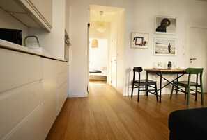 A modern kitchen with white cabinets, a wooden floor, and a dining area with two chairs and a table.