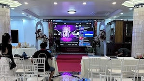 Un evento formal con un escenario, sillas blancas y una araña de cristal.