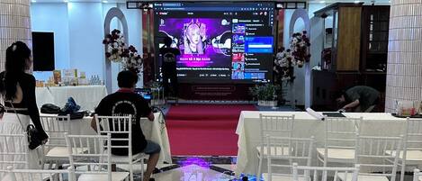 Un evento formal con un escenario, sillas blancas y una araña de cristal.