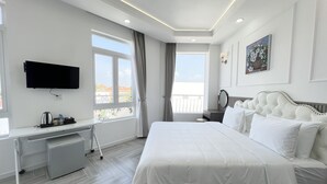 Una habitación de hotel moderna con una cama grande, un escritorio con televisión de pantalla plana, un balcón con vistas y un cuadro en la pared.